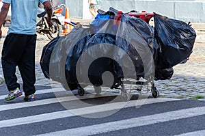 Homeless male dragging a shopping cart full of different items in black bags
