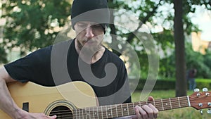 Homeless man with belongings on the street sitting on parapet, playing guitar