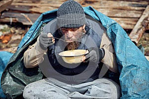 A homeless man eats soup from a plate near the ruins, helping poor and hungry people during the epidemic
