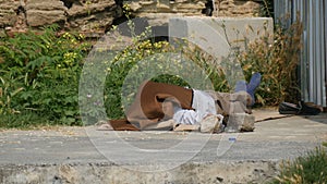 Homeless man lies and sleeps on the street under fence covered with material from sun