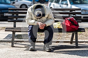 Homeless man, Poor homeless man or refugee sleeping on the wooden bench on the urban street in the city with bags of clothes and j