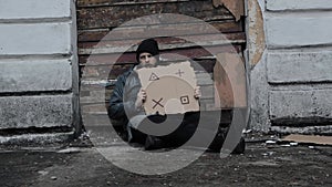 Homeless man sits holds piece of cardboard with markers for planar tracking. Immigrant. Below poverty line. Refugee