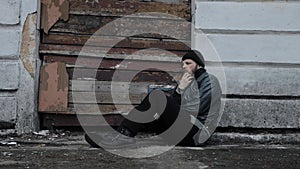 Homeless man sits outside an abandoned building. Consequences of drunkenness alcoholism. Tramp wearing in dirty clothes