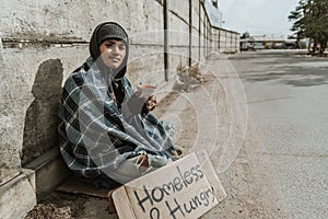 Homeless man sitting on the street in the shadow of the building and begging for help and money. Problems of big modern cities