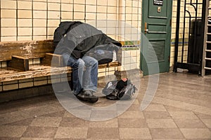 Homeless man sleeping on the bench in New York City subway station covered by own coat