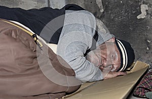 Homeless man sleeping on cardboard and an old sleeping bag o