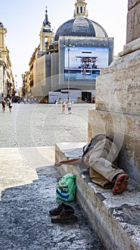 Homeless man sleeps on the street in the shadow of the Egyptian obelisk at Piazza del Popolo