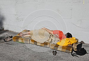 Homeless man sleeps on a worn mattress on the street waiting for