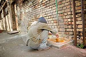 Homeless man squating to wash hands.