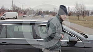Homeless man walks up to car in public parking, male burglar robber looks through slightly open window of auto's