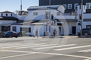 A homeless man wearing a black hoodie pushing a shopping cart and a man crossing a street wearing a black shirt and gray shorts