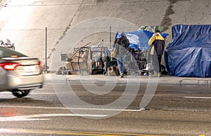 Homeless people at a camp with blue tarp under a bridge during a rain storm