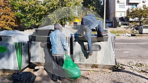 Homeless people seek food and valuables in a trash can. The disadvantaged louis carry a beggarly lifestyle. Sorting municipal