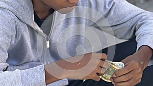 Homeless sad afro-american guy holding last dollar banknotes in palm, poverty