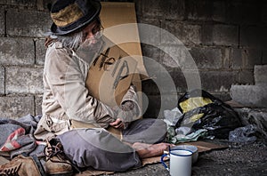 Homeless senior man with gray beard sitting and holding cardboard sign seeking help and beggar on walking street