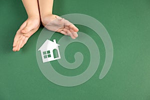 Homeless shelter and real estate concept. Close up of child hands holding white paper house and heart on green background.