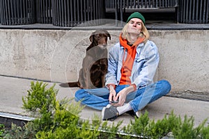 Homeless upset dog sitting on street with hipster guy volunteer in downtown.