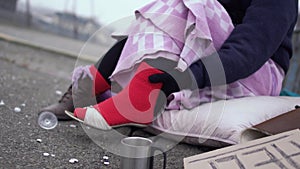 Homeless woman appreciate the shoes worn on a thick red sock outdoors.