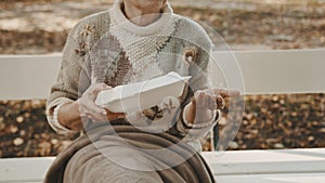 Homeless woman with charity meal and some coins in her hand sitting on the bench in autumn