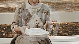 Homeless woman with charity meal and some coins in her hand sitting on the bench in autumn