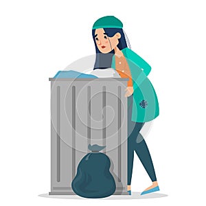 Homeless woman in dirty clothes standing at the trash can