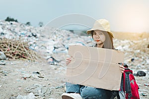 Homeless woman holding sign with hat and backpack sitting on a road