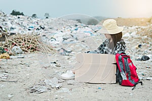 Homeless woman holding sign with hat and backpack sitting on a road