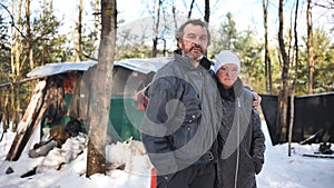 A homeless woman and a man pose in the woods in winter.