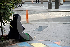 homeless woman with placard and plastic cup sitting in the street