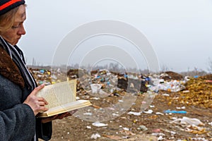 Homeless woman reads a book on the background of a junkyard