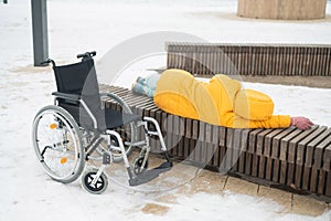 Homeless woman sleeping on a park bench next to a wheelchair.