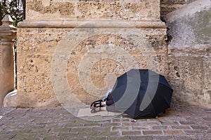 A homeless woman sleeps on the floor at the entrance to the cathedral in Malaga, Spain, covered by a black umbrella