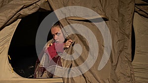 Homeless woman in tent looking out, trembling from cold at night, shelter