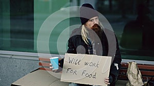 Homeless young man beg for money shaking cup to pay attention people walking near beggar at the city sidewalk