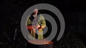 Homeless young man stands by the fire. A man stands at night near a barrel of fire and bask.