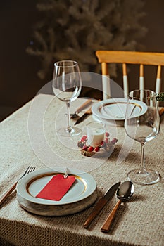 Homely christmas table setting, decorated with pine branches and rustic tablecloth in the living room of home tree lit background