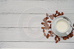 Homemade almonds milk in a white ceramic mug and pile of roasted almonds placed on white wooden background.