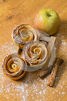 Homemade apple cakes with cinnamon and icing sugar on wooden background. Apple Rose mini tarts