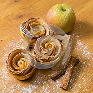 Homemade apple cakes with cinnamon and icing sugar on wooden background. Apple Rose mini tarts