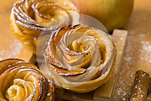 Homemade apple cakes with cinnamon and icing sugar on wooden background. Apple Rose mini tarts