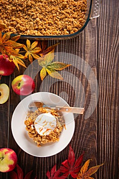 Homemade apple crumble crisp cake on white plate with autumn leaves on the wooden background