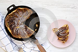 Homemade Apple Dutch Pannekoek Pancake in a cast-iron pan on a white wooden background, top view