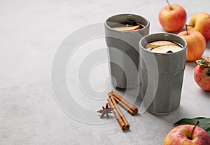 Homemade apple punch with apples and cinnamon in gray cups on a light background with fresh fruits and spices. The concept of an