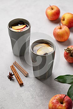 Homemade apple punch with apples and cinnamon in gray cups on a light background with fresh fruits and spices. The concept of an