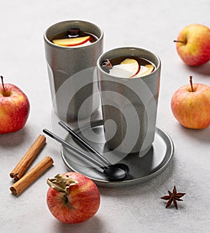 Homemade apple punch with apples and cinnamon in gray cups on a light background with fresh fruits and spices. The concept of an