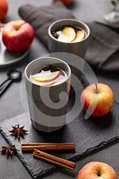 Homemade apple punch or cider with apples and cinnamon in gray cups on a dark background with fresh fruits and spices close up