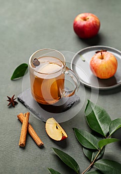 Homemade apple punch with fresh apples, cinnamon and spices in cup on a green background with fresh fruits and branch. A hot