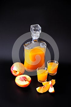 Homemade apricot liqueur in two glasses and a glass decanter, next to pieces of ripe fruit on a black background