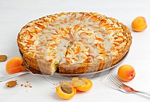 Homemade apricot pie with gooseberry and frangipane decorated with almond petals on white wooden table.