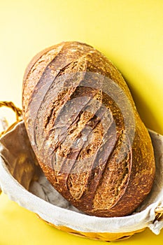 Homemade artisanal sourdough bread in a bread basket. Yellow background. Healthy home baking concept